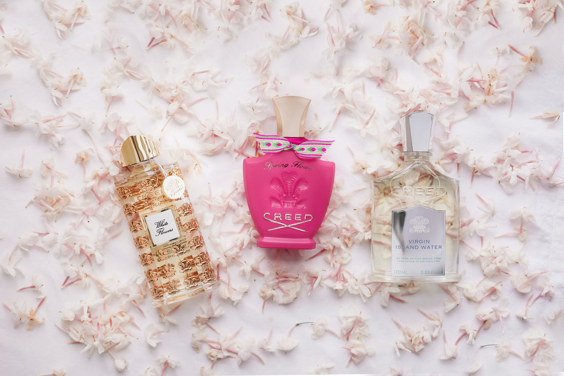 Creed Spring Flower, Creed White Flowers y Creed Virgin Island Water sobre una cama de pétalos rosas.